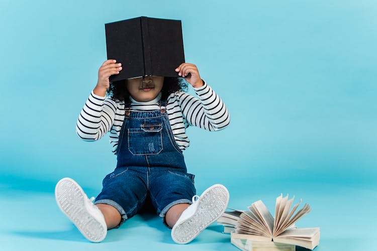 Small Black Girl Sitting On Floor With Books In Studio