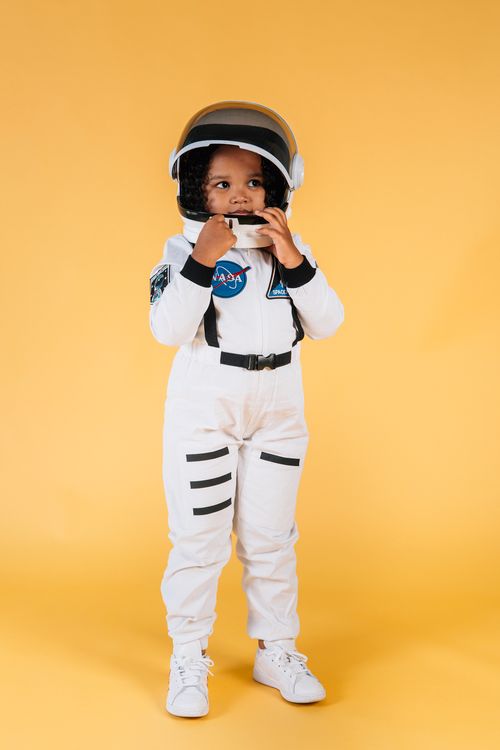 Free Adorable child dressed as an astronaut in a studio with a vibrant yellow background. Stock Photo