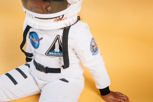 Crop anonymous African American child wearing white space suit and helmet with NASA logo on orange background