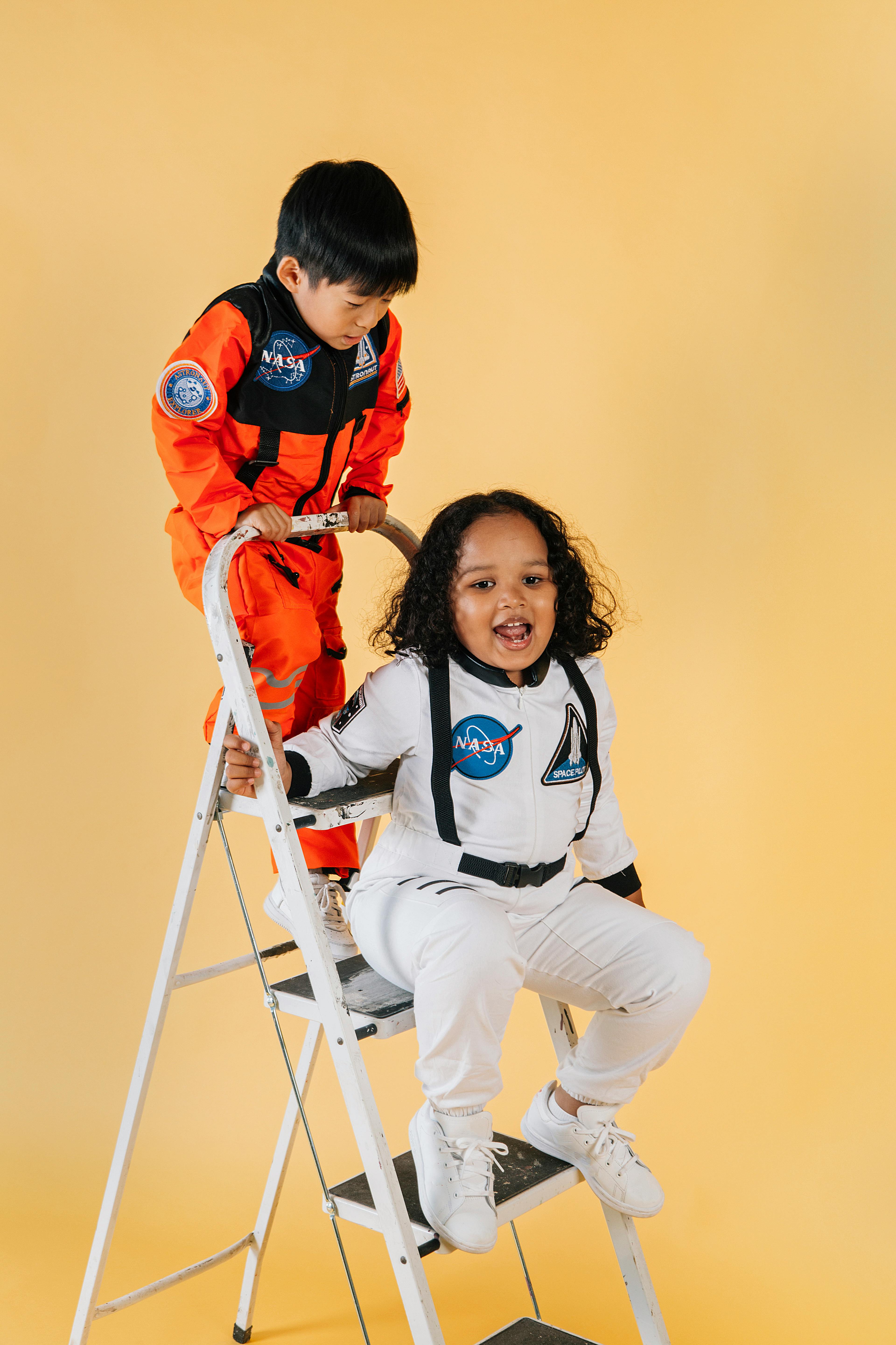 cheerful multiethnic children in astronaut costumes on ladder in studio