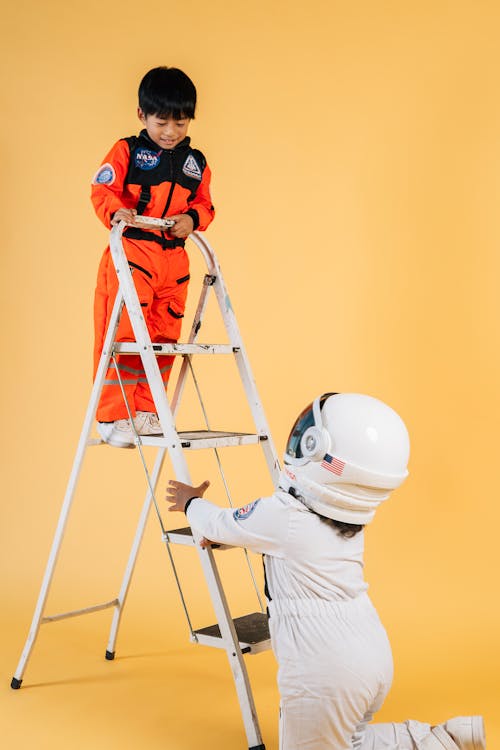 Children in astronaut costumes playing on ladder in studio