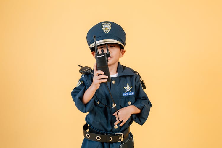 Asian Boy In Police Uniform Against Yellow Background