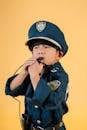 Focused ethnic kid in police uniform costume blowing whistle while standing in photo studio on yellow background and looking away