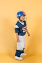 一个身穿美式足球运动员制服、戴着头盔的亚洲男孩，站在黄色背景的演播室里，望向远处