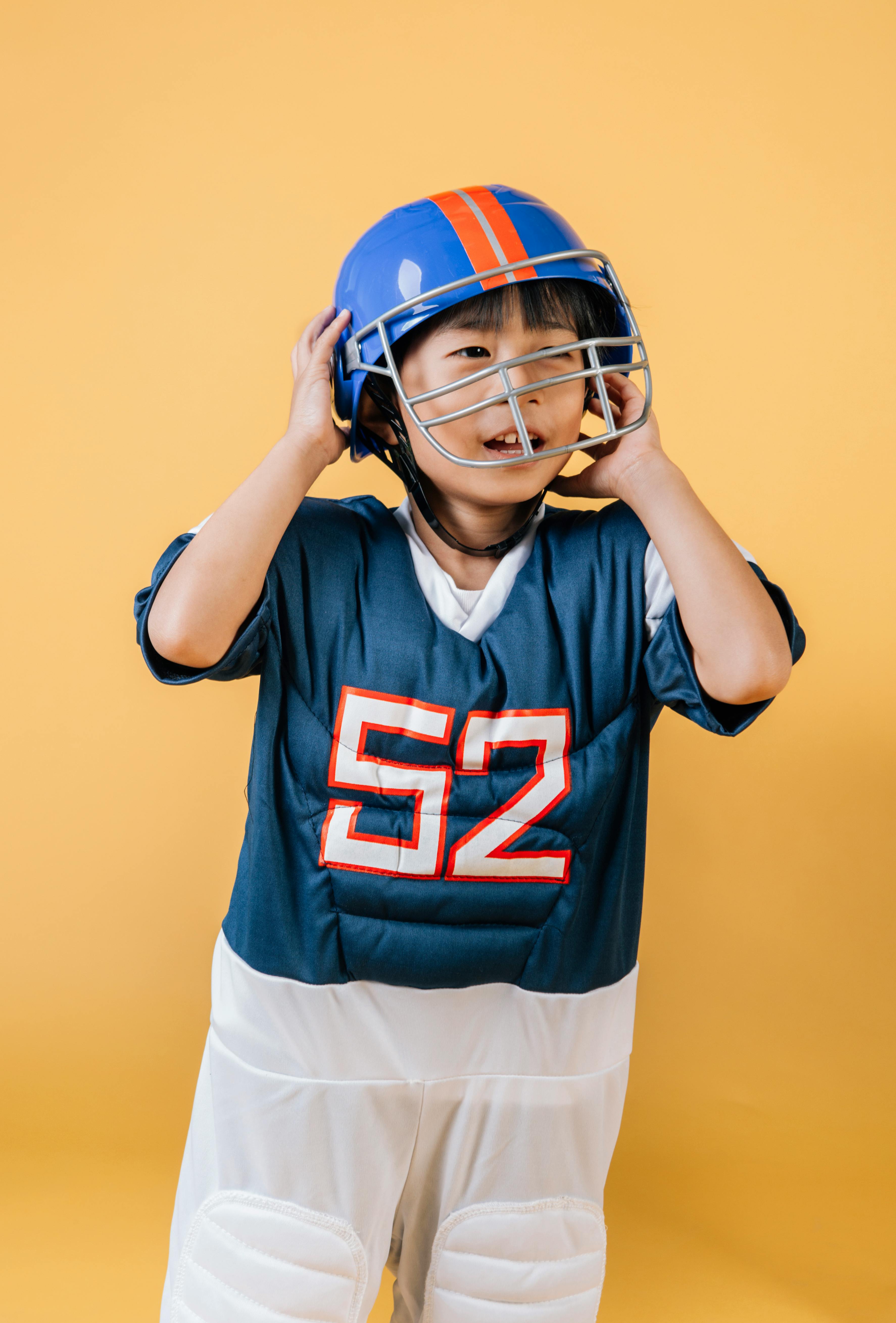 asian kid in american football player outfit taking off helmet