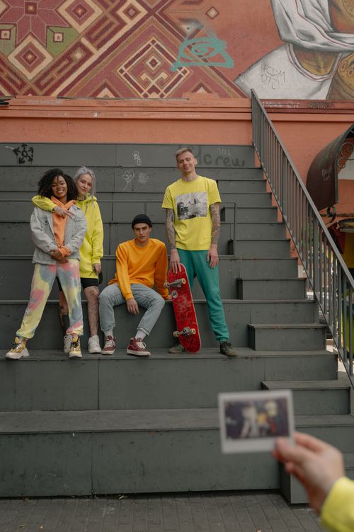 Free Group of trendy friends in colorful outfits posing on urban steps with skateboard, captured in street style. Stock Photo