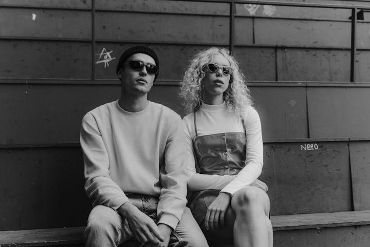 Young Man And Woman In Trendy Outfits Sitting By The Wall 