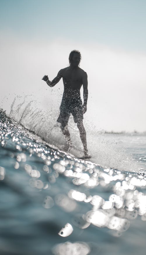 Full body of male surfer practicing surfing on glow blue sea under clear sky