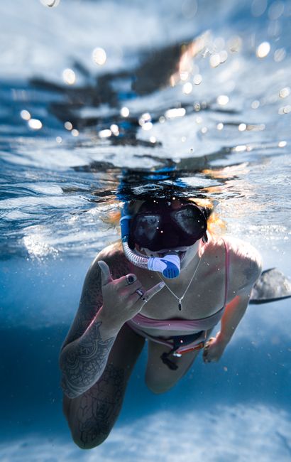 Underwater view of fit cheerful female in snorkeling mask and goggles swimming in blue seawater and demonstrating love gesture