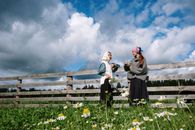 两个戴头巾的女人在乡村篱笆旁聊天，篱笆外是一片开满鲜花的草地