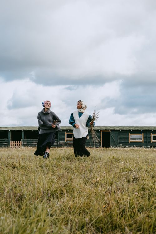 Free Two women walking across a grassy field in front of a barn under a cloudy sky. Stock Photo