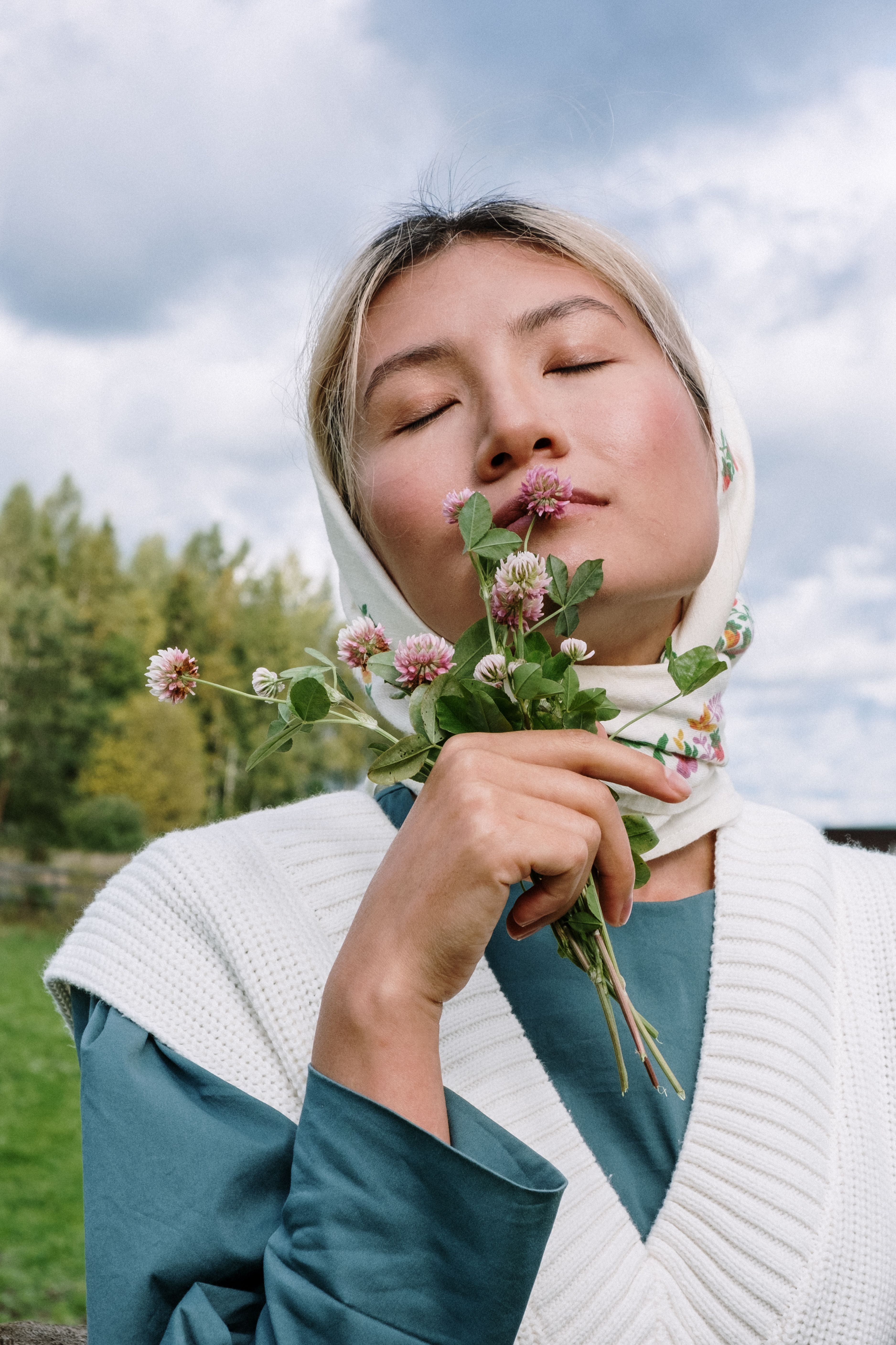 Asian woman outdoors with eyes closed, holding flowers, embodying tranquility.