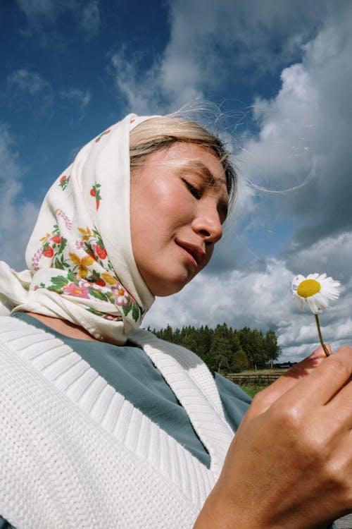 Young Woman Wearing a Headscarf Standing on a Meadow and Holding a Flower