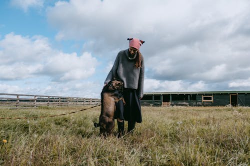 Woman in Gray Sweater and a Dog Standing on Grass Field 