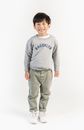 Full body joyful little Asian boy in cool outfit standing against white wall and looking at camera with happy smile
