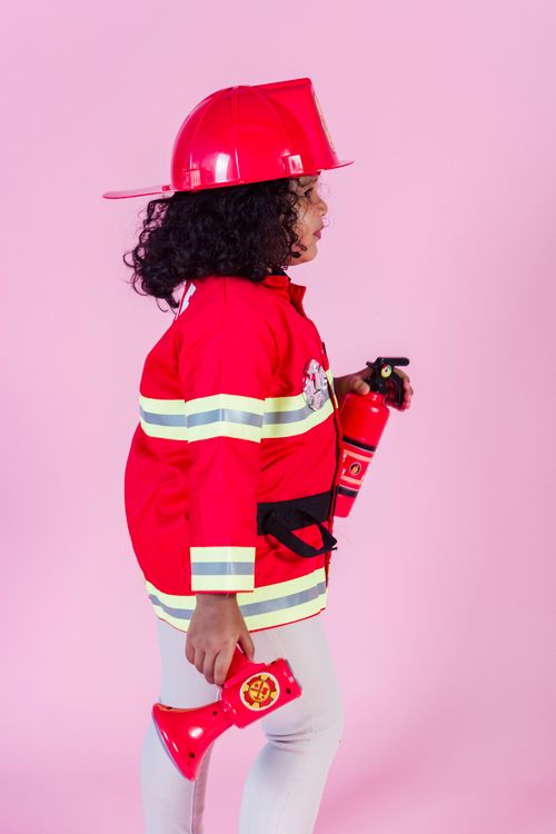 Free Child dressed as firefighter with helmet, posing in studio against pink background. Stock Photo