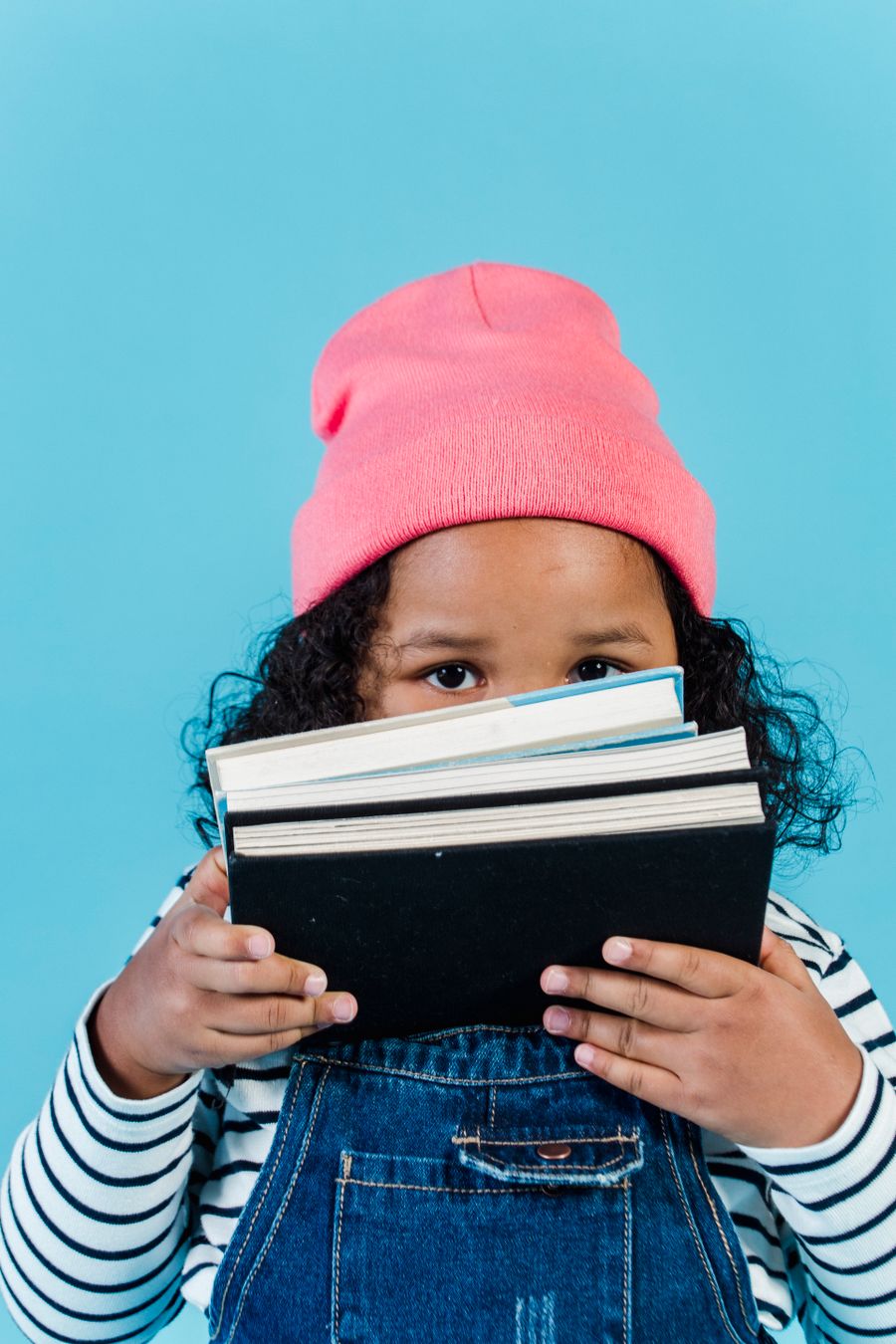 A young Black reader in a pink cap holding a stack of books