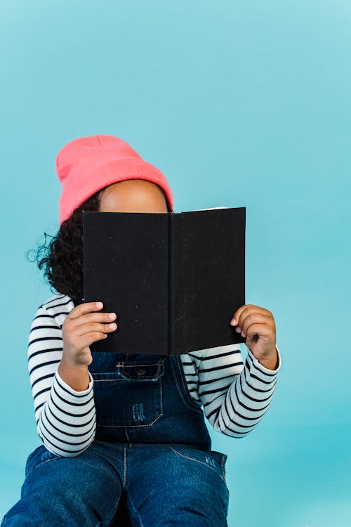 Free Faceless curious girl reading book and hiding face Stock Photo