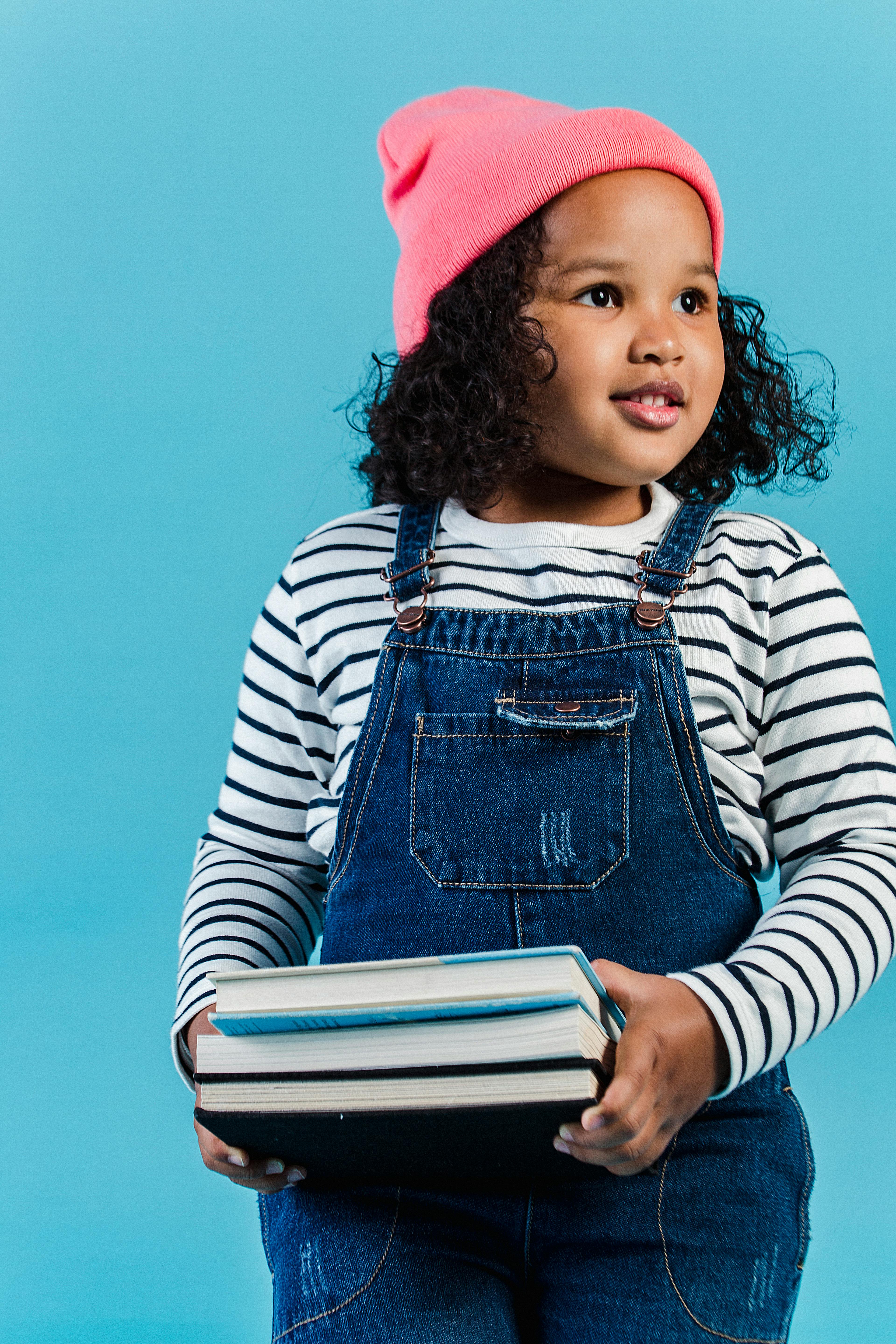 glad stylish black girl standing with stacked books in hands