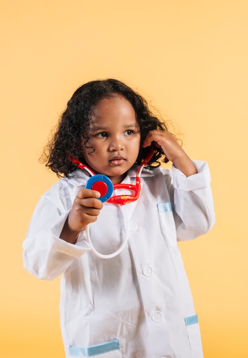 Little black girl in medical robe playing with toy stethoscope
