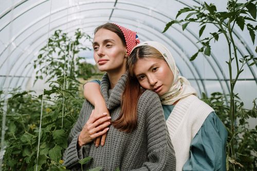 Free Two young women embracing inside a lush greenhouse, surrounded by plants. Stock Photo