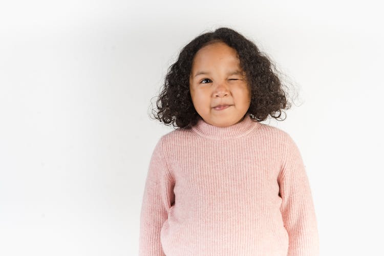 Adorable African American Kid Winking At Camera In White Studio