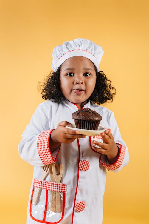 A Kid in Chef Uniform holding a Saucer with Chocolate Cupcake