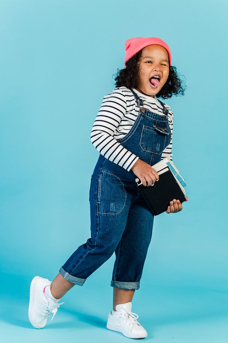 Joyful Black Girl With Textbooks Grimacing In Studio