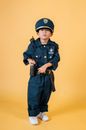 Full length adorable little Asian boy wearing policeman uniform and cap and looking at camera while standing on yellow background