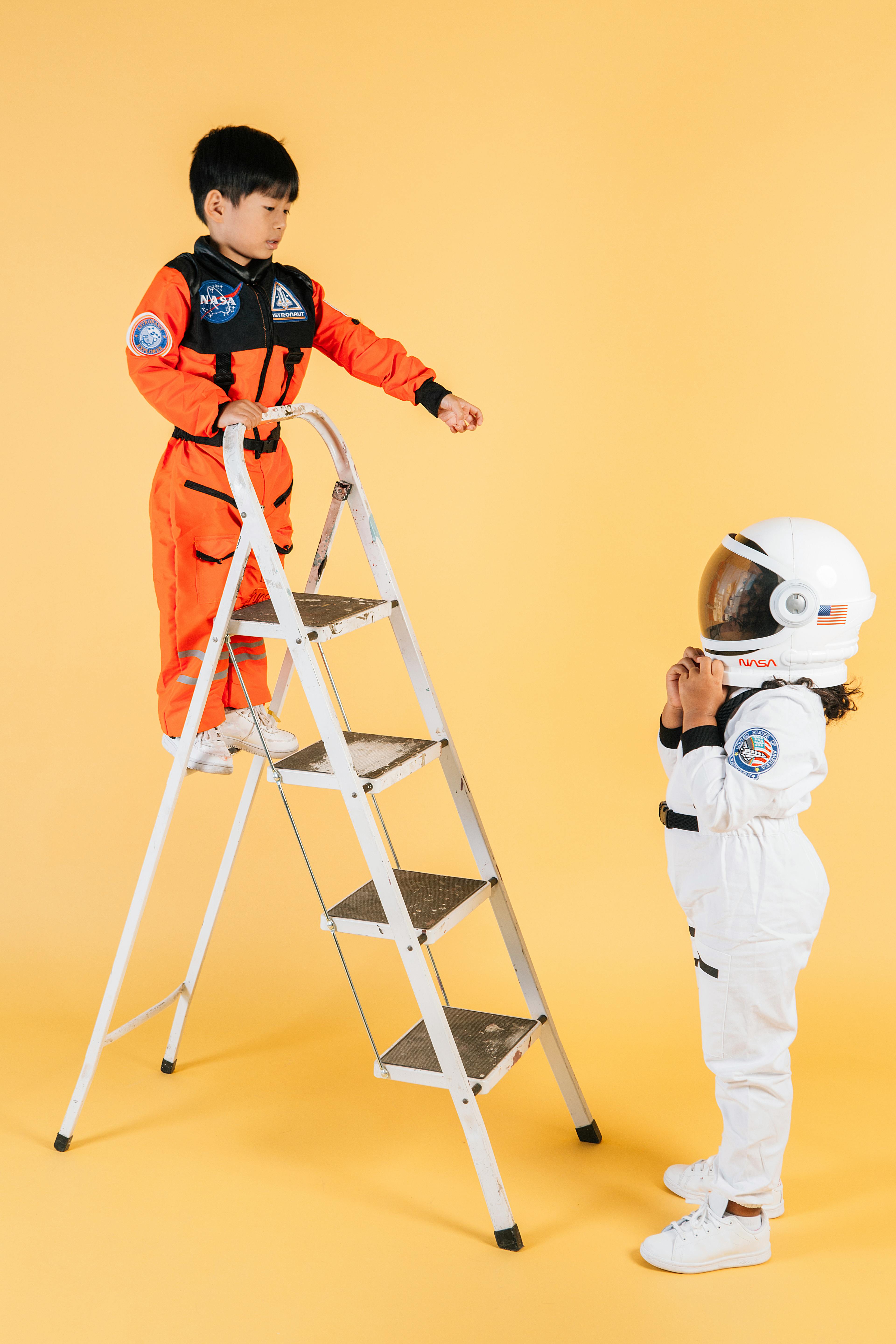 little ethnic children in cosmonaut costumes playing on ladder