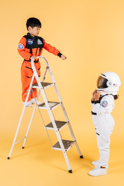 Little ethnic children in cosmonaut costumes playing on ladder