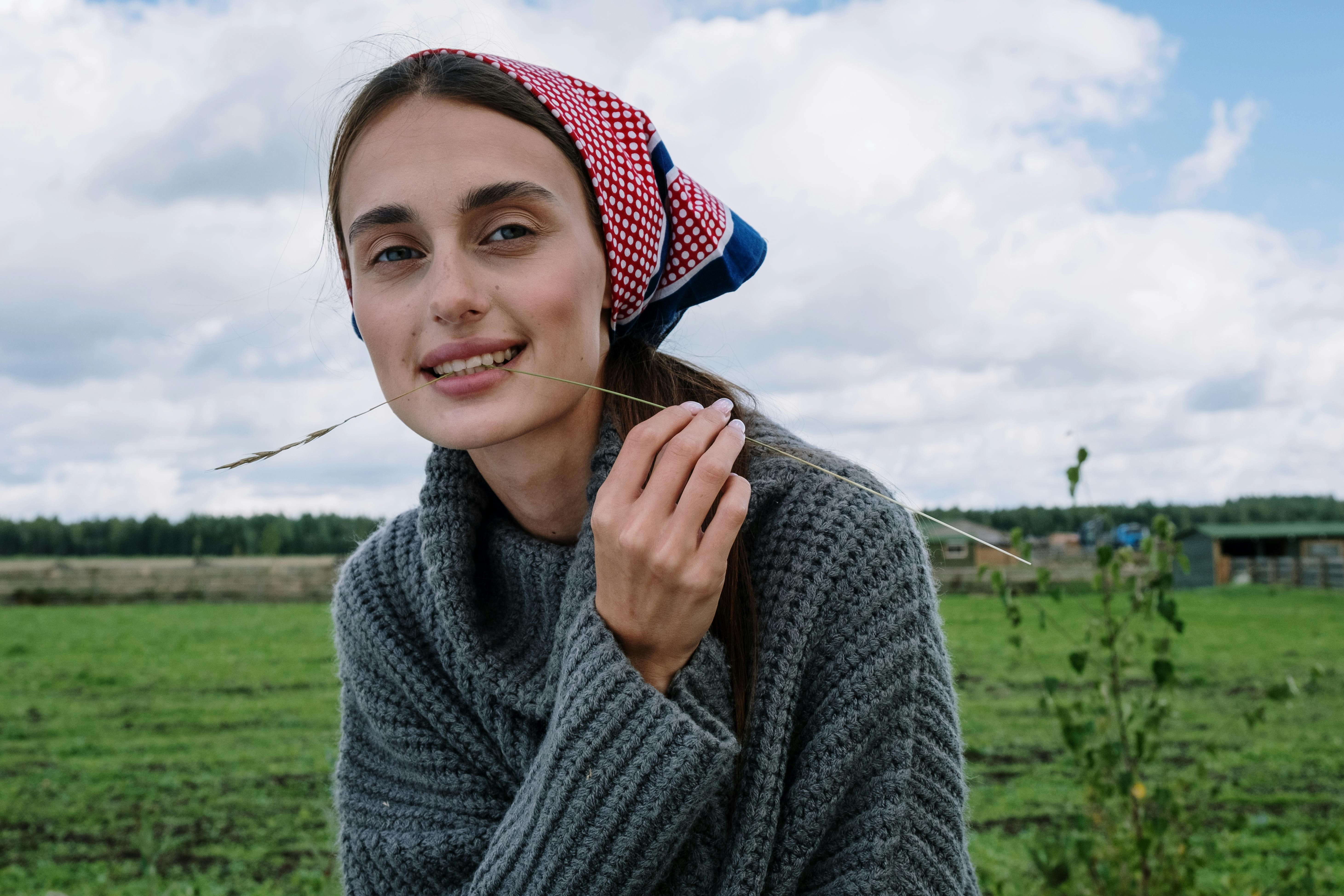 woman in gray sweater biting a grass stalk