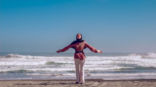 Free A woman enjoys the ocean breeze on a sunny Indonesian beach, expressing joy and relaxation. Stock Photo
