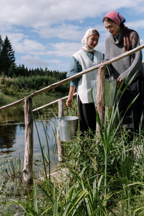 Free Two women gather water by a riverside in a rustic rural setting. Stock Photo