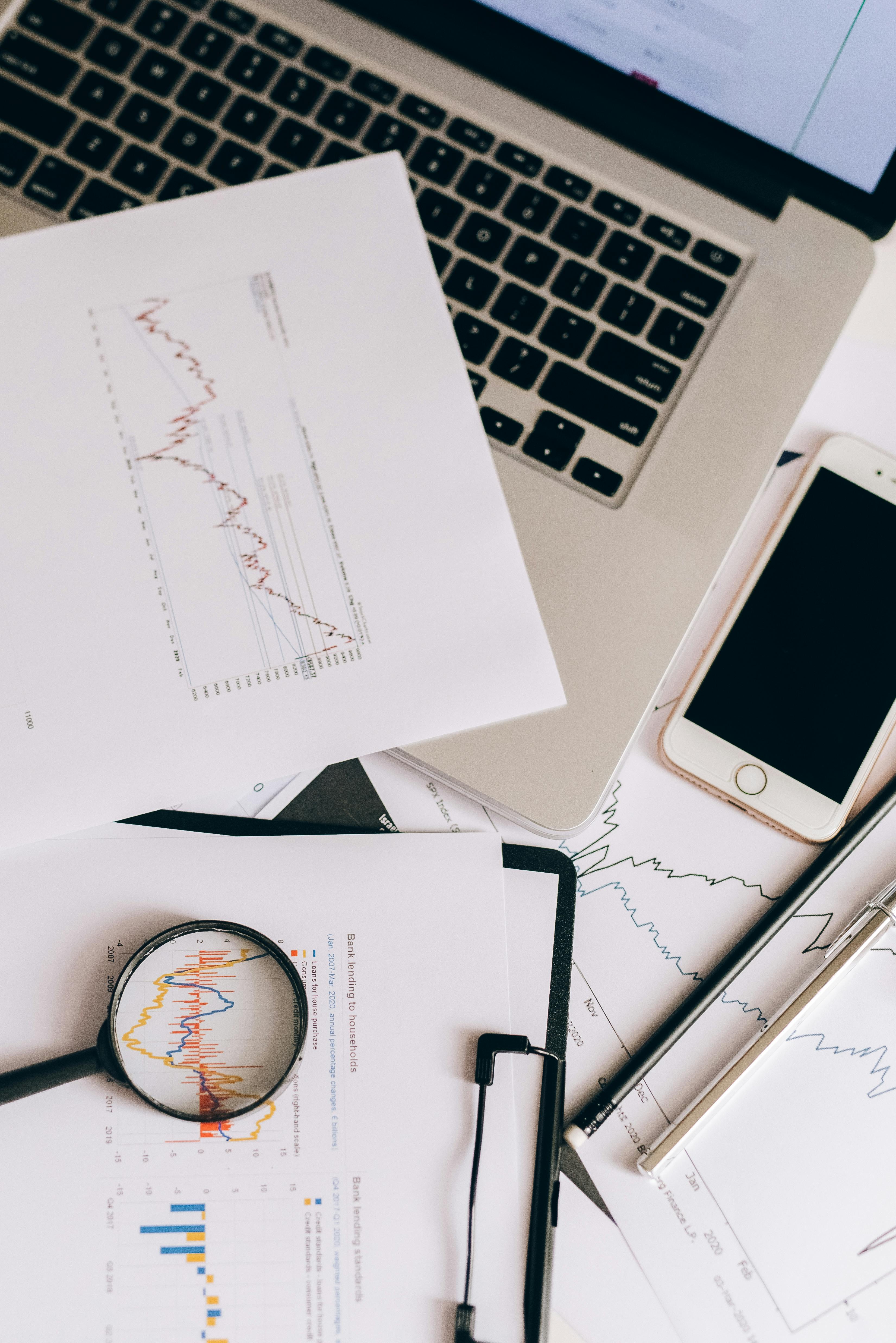 papers with statistics beside a laptop and smartphone