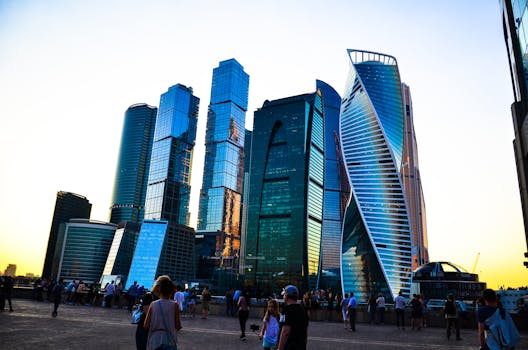 在繁华的城市景观中，现代摩天大楼映照着充满活力的日落，人们聚集在下方