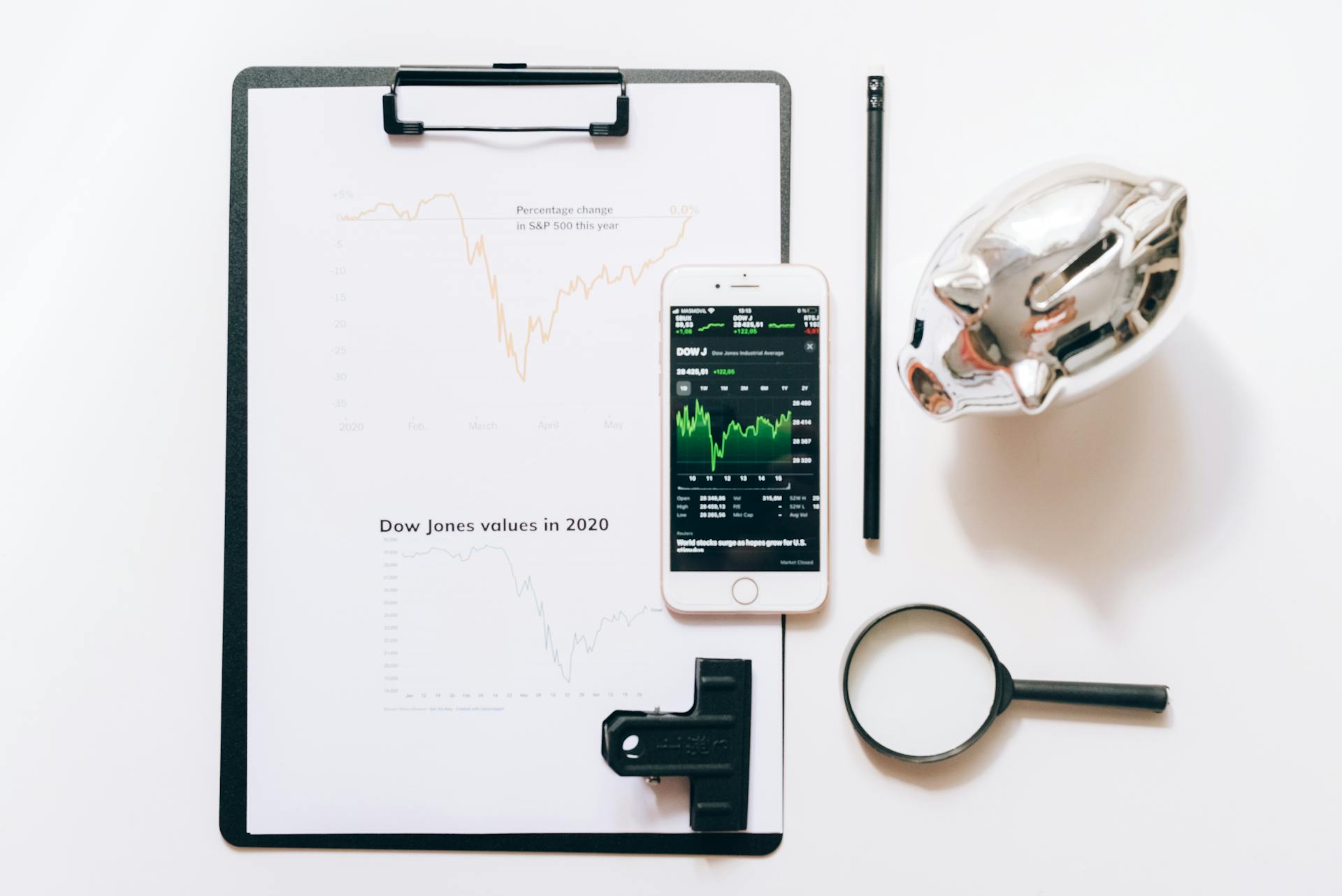 A Cellphone on Top of Clipboard Beside Magnifying Glass and Piggy Bank