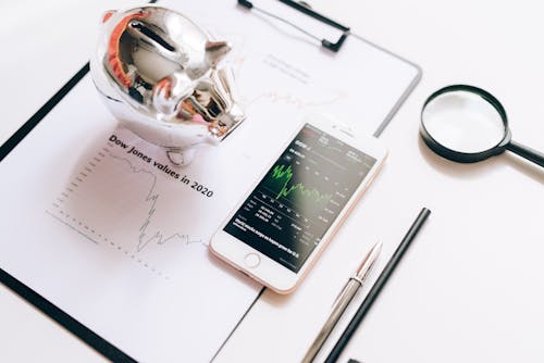 Smartphone Displaying a Stock Market Chart and Lying on a Document next to a Magnifying Glass