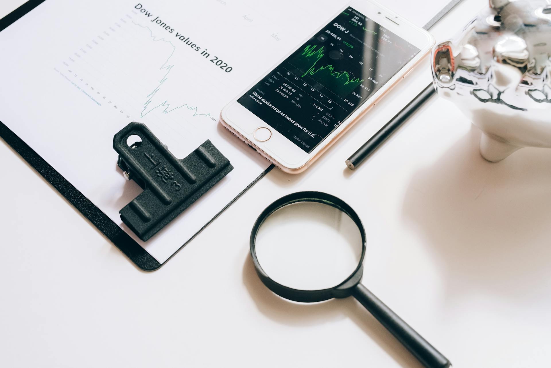 Smartphone Displaying a Stock Market Chart and Lying on a Document next to a Magnifying Glass