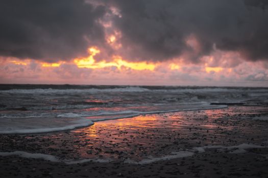 Dramatic clouds and vibrant sunset reflecting on a rocky shoreline, creating a vivid seascape.