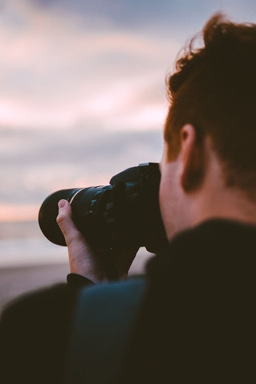 Man in Black Jacket Holding Black Dslr Camera during Sunset