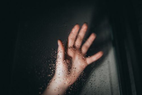 Free A hand reaching out against a window with water droplets on a cloudy day. Stock Photo