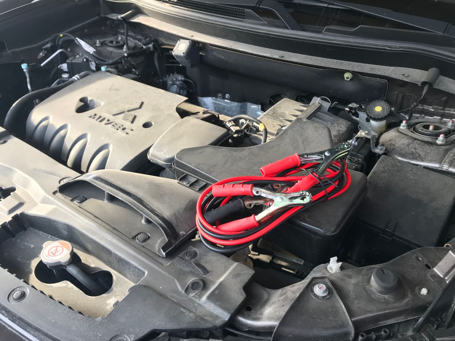 Blick in den Motorraum mit angeschlossenen Starthilfekabeln bei einer Prüfung.