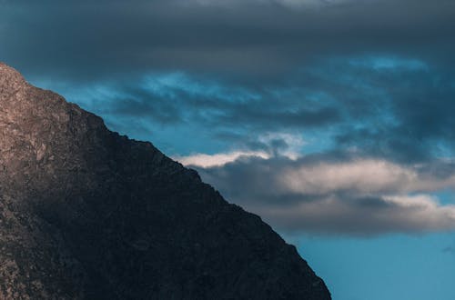 Picturesque view of mountain range with rough rocky surface under blue cloudy sky