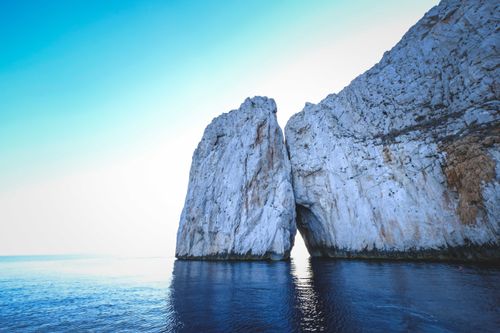 Free Amazing view of rough rocky cliffs in rippling ocean water under blue sky with sunlight Stock Photo