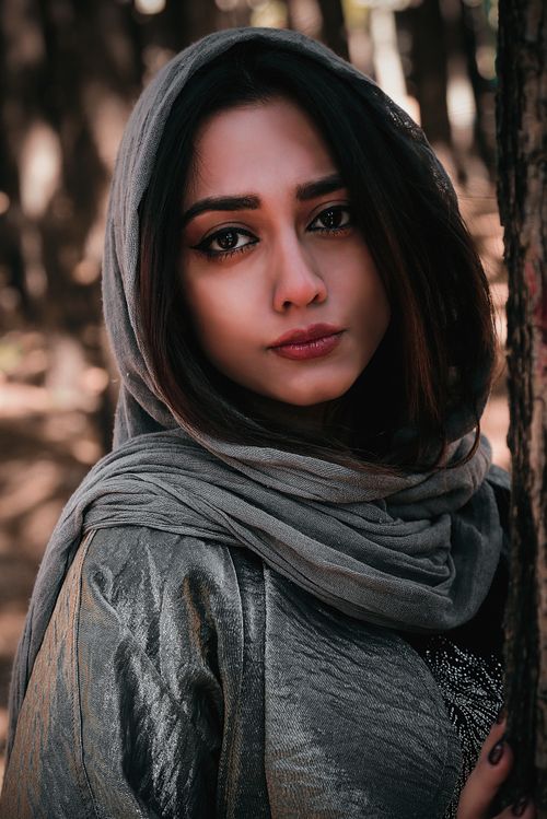 Free Captivating portrait of a woman wearing a scarf in a serene forest setting, exuding elegance and mystery. Stock Photo