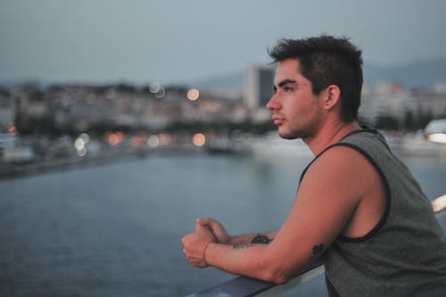 Side view of young tattooed male standing on bridge over river and looking away
