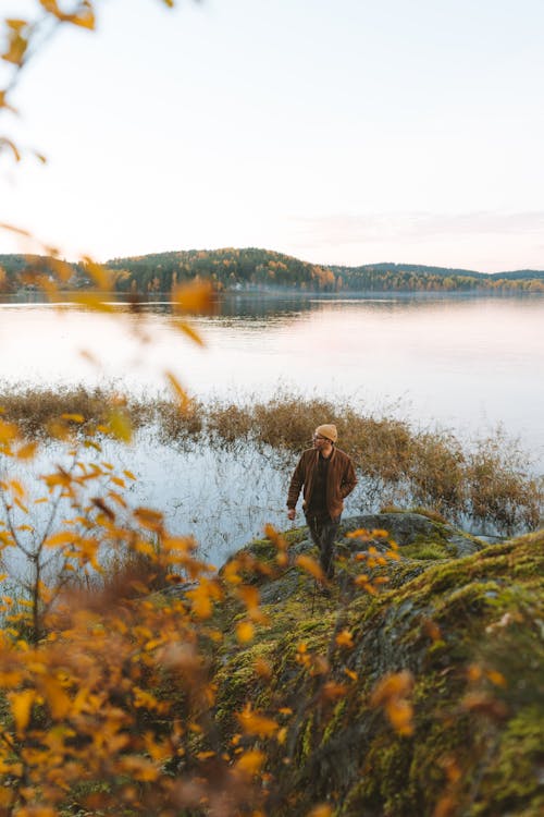 Free Person in Brown Jacket walking on Boulder on a Lakeside during Autumn  Stock Photo