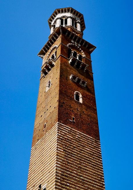 Low angle of the landmark Scaliger Tower in Verona, Italy, with a clear blue sky backdrop.