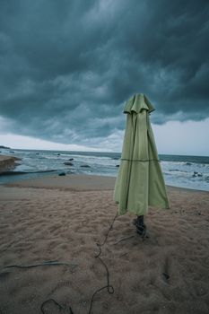 一把绿色的封闭雨伞立在多云天空下的沙滩上